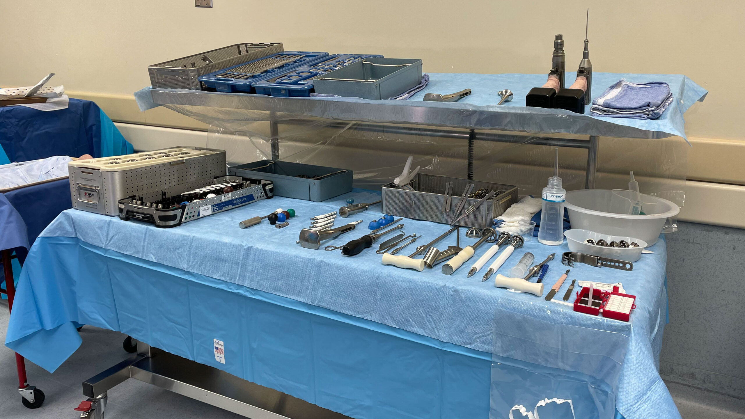 two-tier surgical back table in operating room set up with a blue sterile drape and surgical instruments