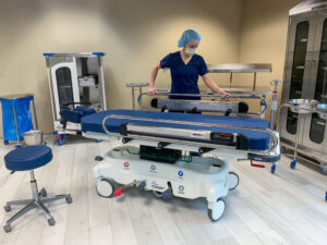 One person in blue scrubs behind a Pedigo Products stretcher in an operating room
