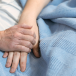 two hands holding in hospital bed on blue blanket