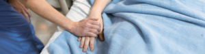 two hands holding in hospital bed on blue blanket